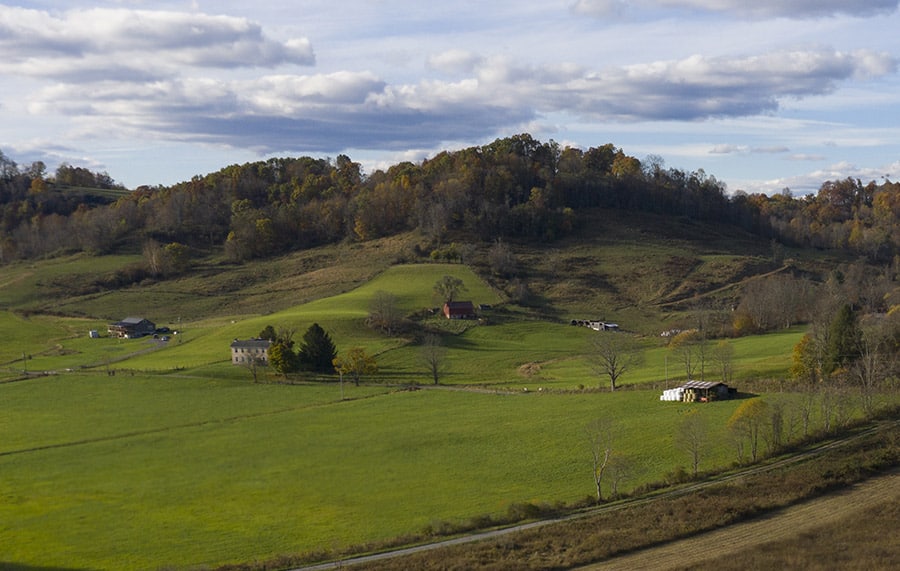 green field with a barn in front of rolling hills with trees